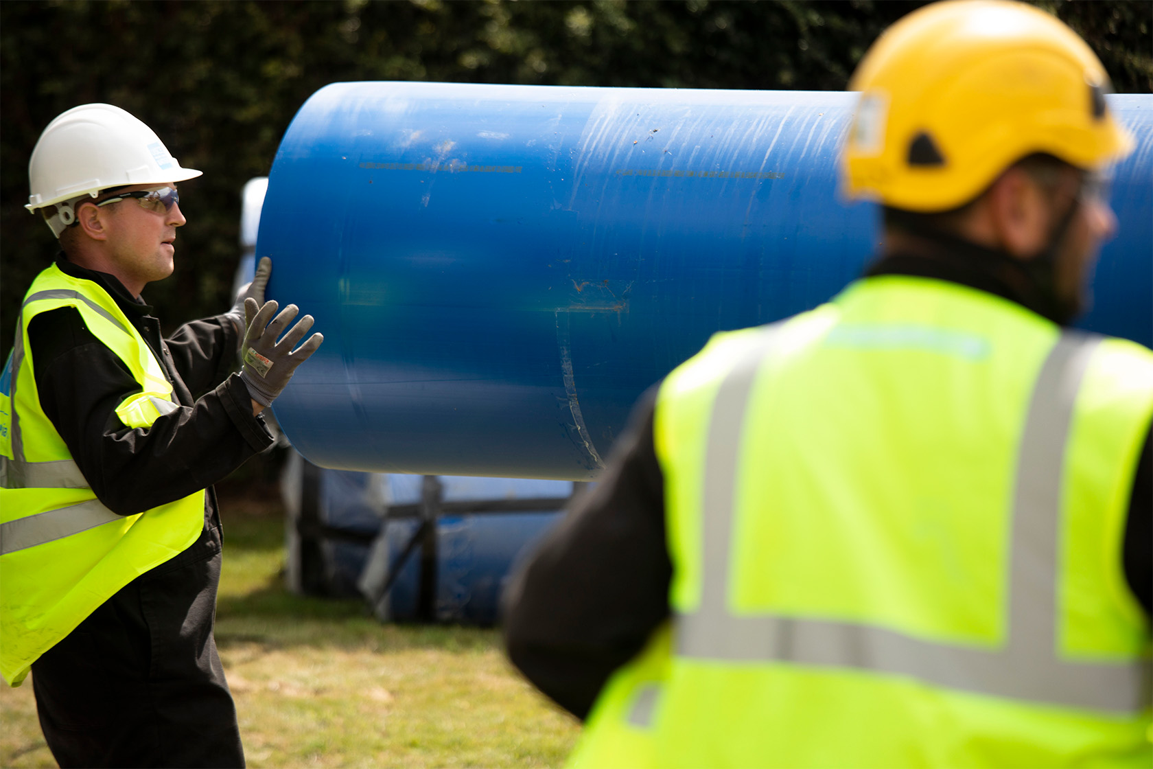 Two engineers holding a large blue pipe wearing safety gears