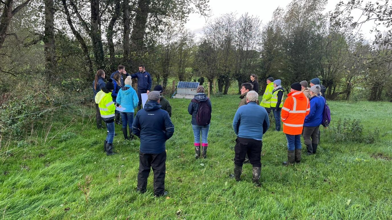 A group of people in a field listening to a person talking making a speach