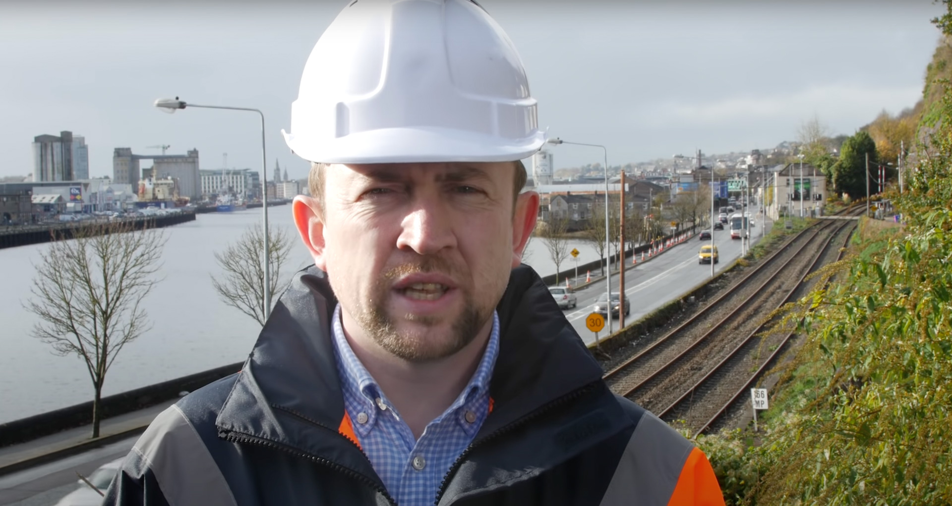 Worker in white helmet in front of train tracks and a town with a river