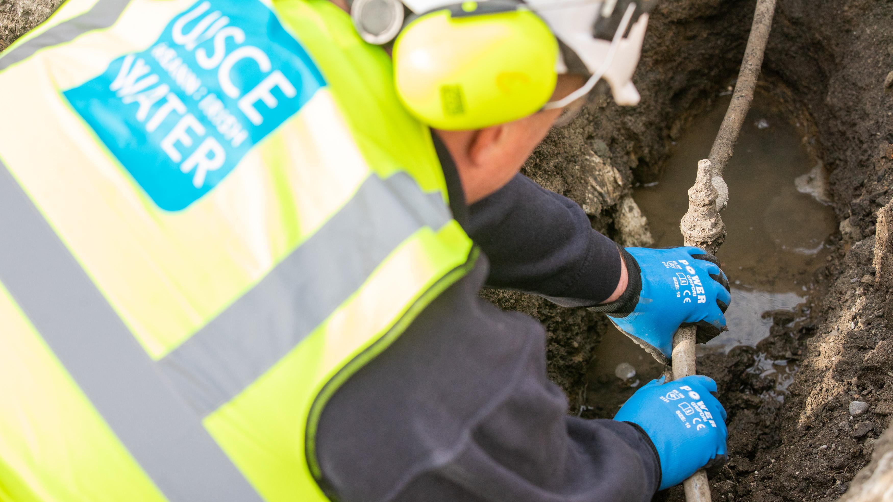 a uisce eireann repairing a pipe in the ground surrounded by dirt