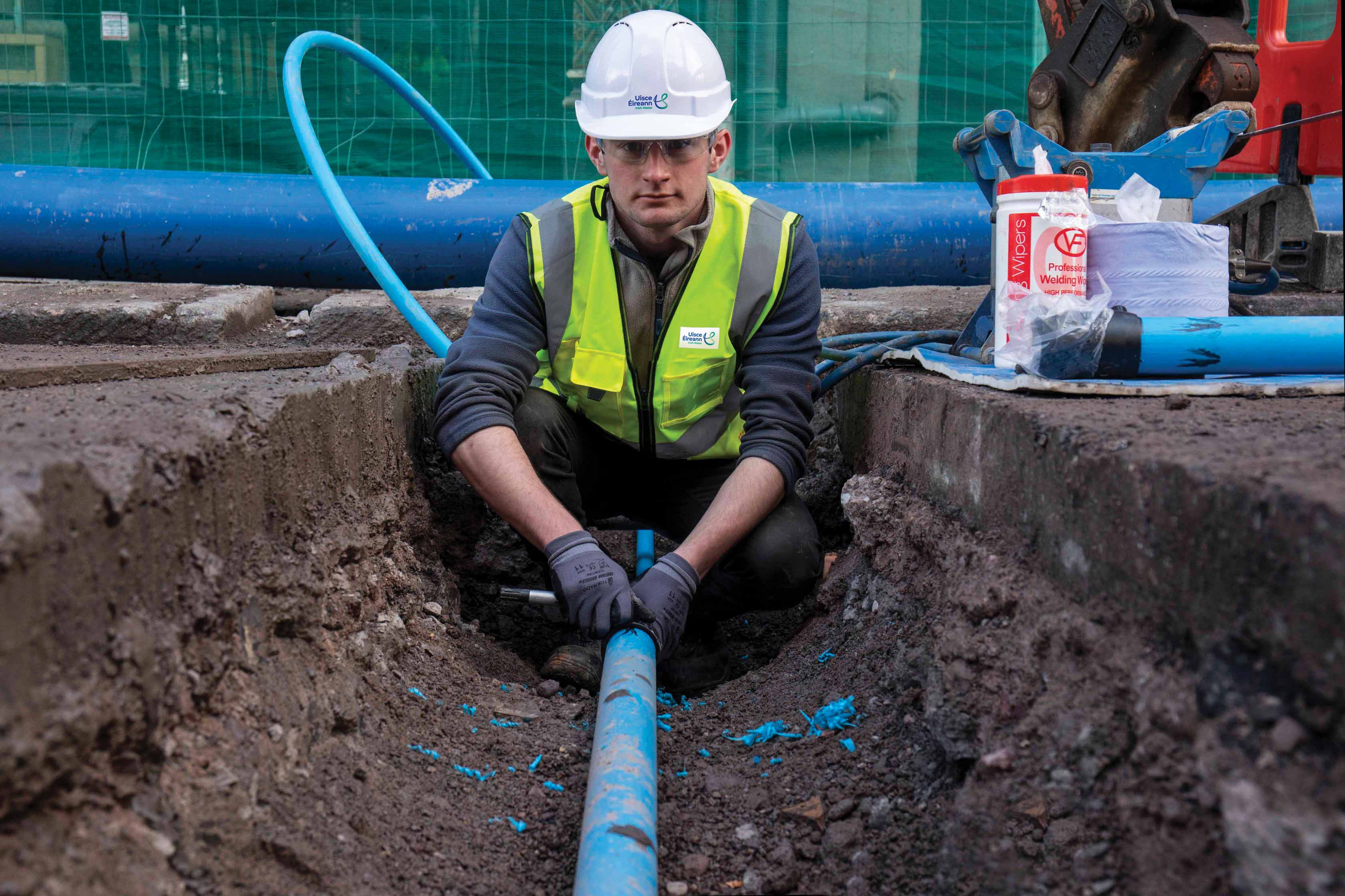 An Uisce Éireann worker fixing a blue pipe in the ground