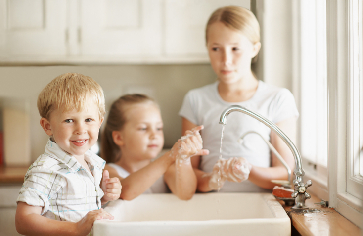 Three kids washing their hands in the sink in a kitchen