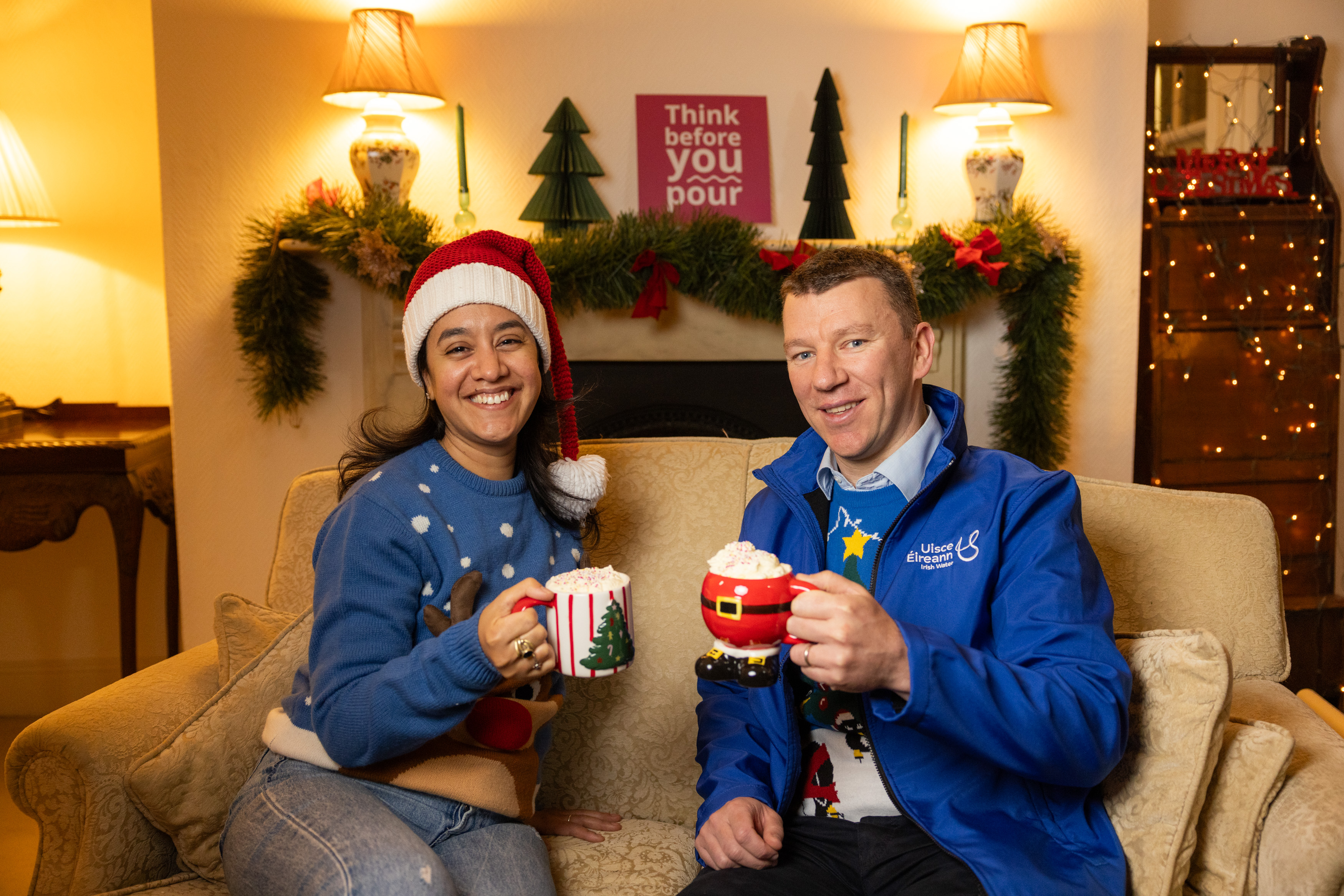 Two Uisce Éireann workers with mugs of hot chocolate and Christmas jumpers on a couch