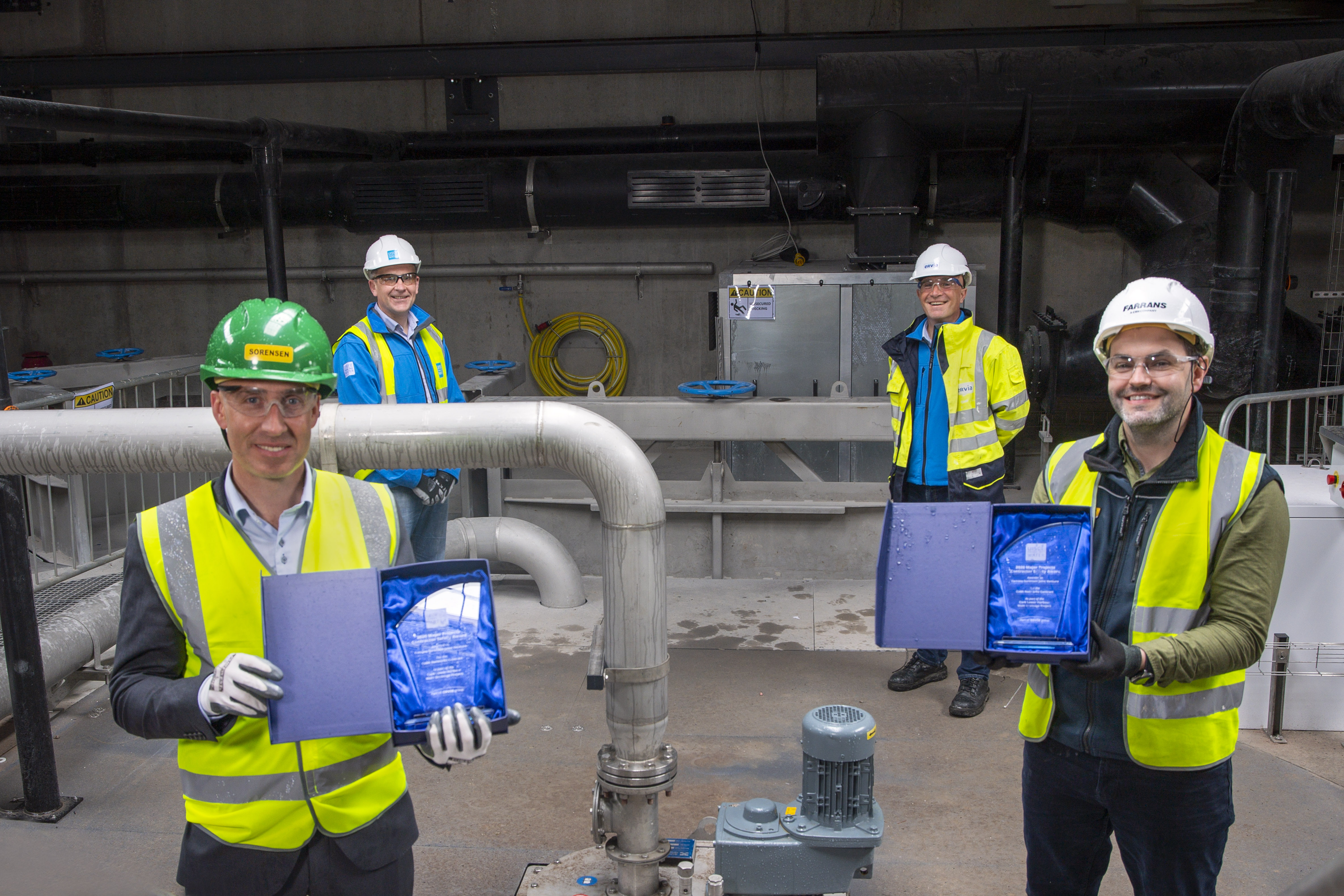 Four workers in hi-vis jackets and hard hats, with two holding glass trophies and smiling