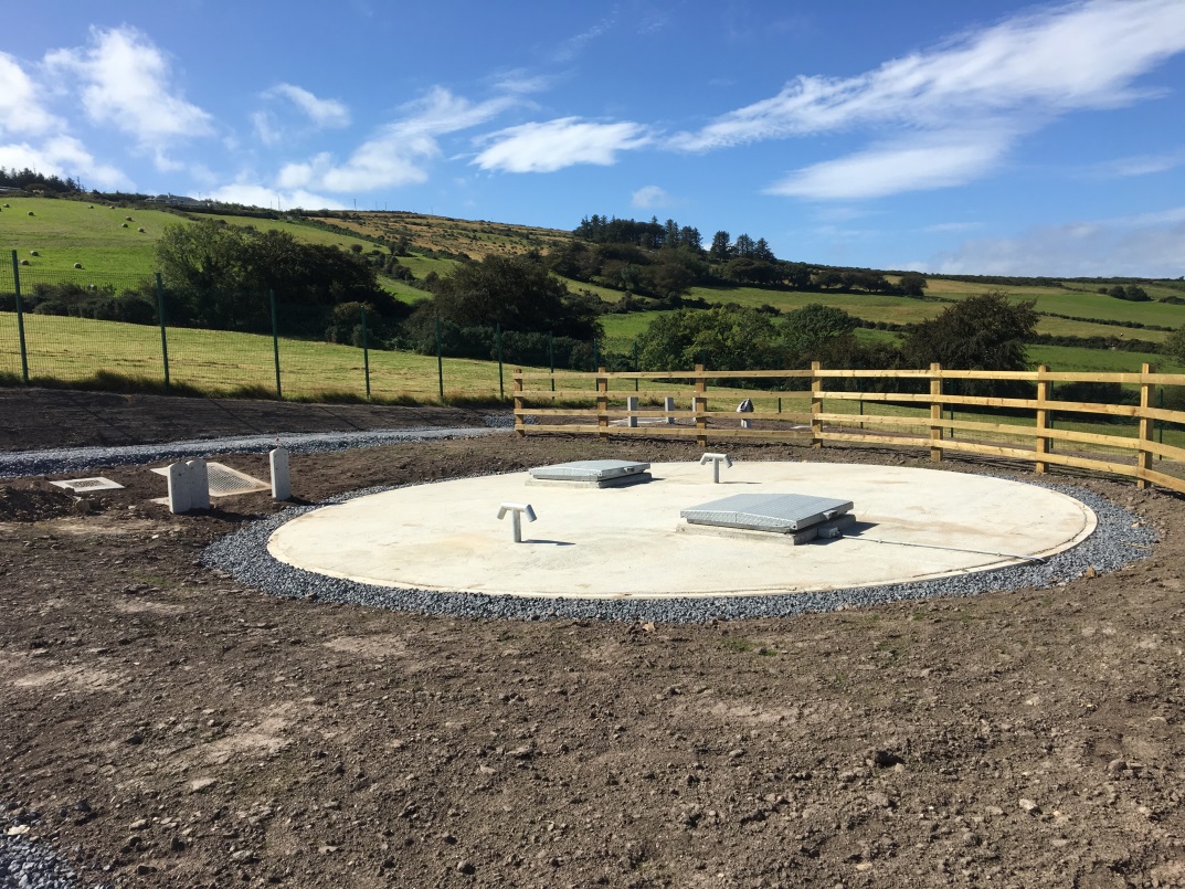 A circular white concrete patch on a plot of dirt with metal squares on it