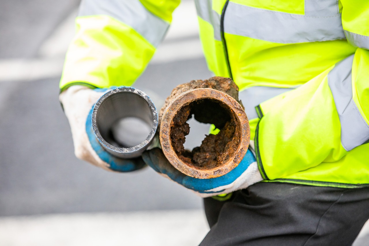 A worker holding a new clean pipe and an old rusty pipe