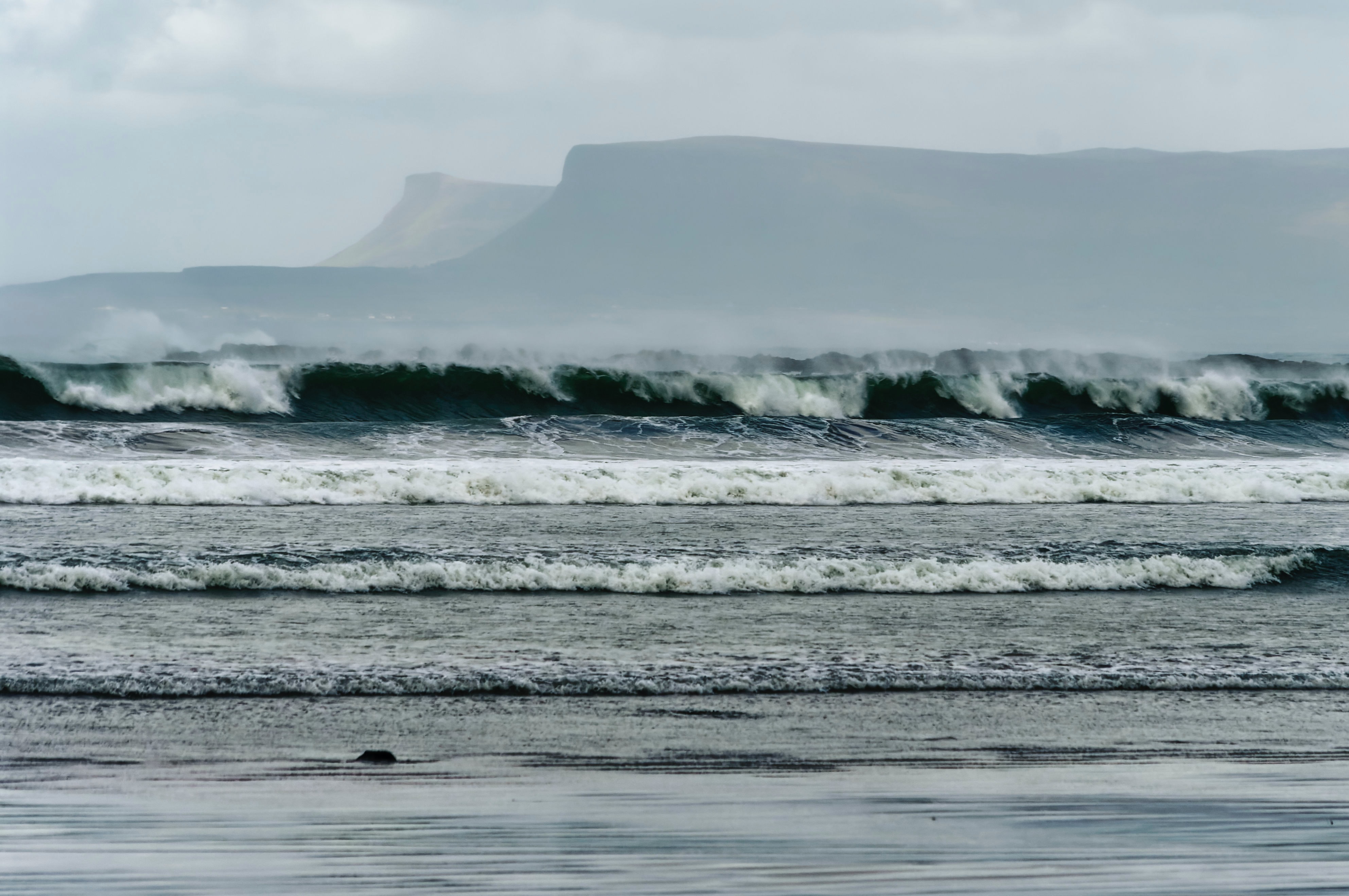 Large waves and mountains in the background covered in mist