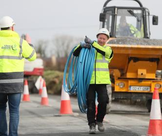 a uisce eireann worker carrying blue pippes over his shoulder giving somebody a thumbs up